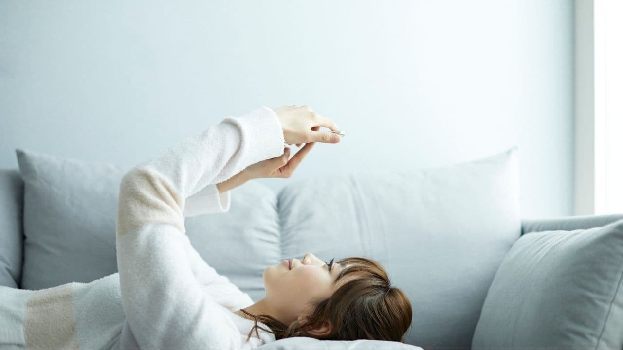 ソファでスマホを触りながらくつろぐ女性の写真